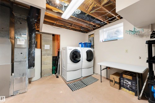 Dedicated laundry area featuring a front-loading washer and dryer, exposed ceiling joists, a small window, and light-colored walls - 10732 129 Street Nw, Edmonton, AB - Indoor Photo Showing Laundry Room