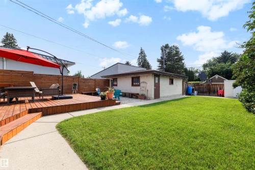 Expansive backyard featuring a spacious wood-decked patio with built-in wooden privacy screens, a large green lawn, a detached garage, and a separate storage shed - 10732 129 Street Nw, Edmonton, AB - Outdoor With Exterior