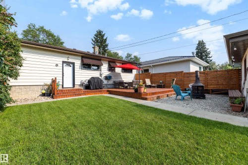 Expansive backyard featuring a large wood deck, a spacious lawn area, a gravel patio with a fire pit, and privacy fencing - 10732 129 Street Nw, Edmonton, AB - Outdoor With Deck Patio Veranda