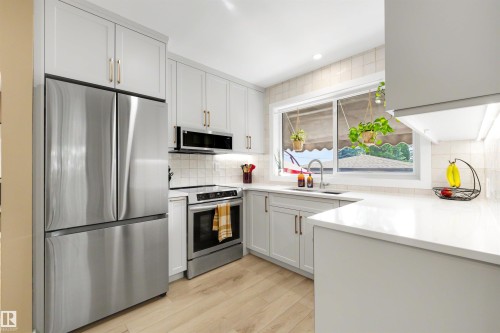 Modern kitchen featuring stainless steel appliances, light wood-finish flooring, white shaker cabinetry with gold-tone hardware, white countertops, and a tiled backsplash - 10732 129 Street Nw, Edmonton, AB - Indoor Photo Showing Kitchen With Upgraded Kitchen