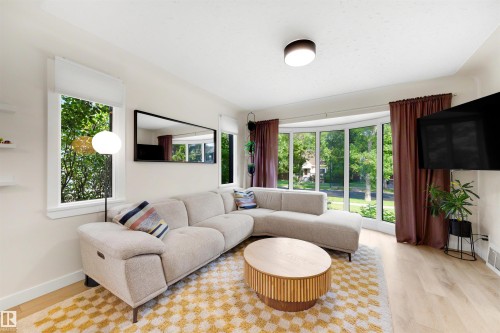 Bright living area featuring wood-finish flooring, a large bay window, and a flush-mount ceiling light fixture - 10732 129 Street Nw, Edmonton, AB - Indoor Photo Showing Living Room