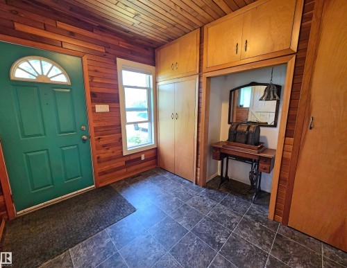Entryway featuring wood-paneled walls and ceiling, a teal door with a half-round transom window, and stone-look tile flooring - 3003 Park Avenue, Mallaig, AB - Indoor Photo Showing Other Room