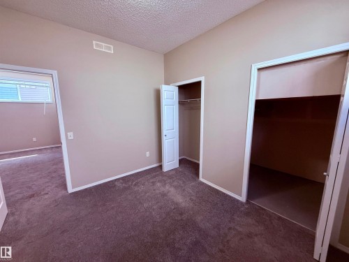 Carpeted interior space featuring neutral tone walls, white trim, a bi-fold closet door, and a sliding closet door - 122 142 Selkirk Place, Leduc, AB - Indoor