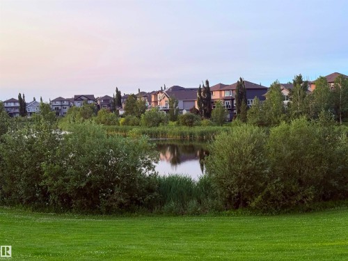 Expansive green space featuring a tranquil pond surrounded by lush foliage and mature trees - 122 142 Selkirk Place, Leduc, AB - Outdoor With View