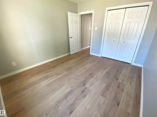 Room featuring wood-finish flooring, light grey walls, white baseboards, and a bi-fold closet with white paneled doors - 12010 66 Street Nw, Edmonton, AB - Indoor Photo Showing Other Room