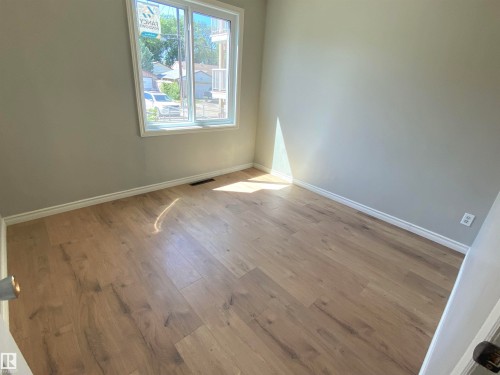 Bright room featuring a large window, light wood-finish flooring, neutral gray walls, and white baseboards - 12010 66 Street Nw, Edmonton, AB - Indoor Photo Showing Other Room