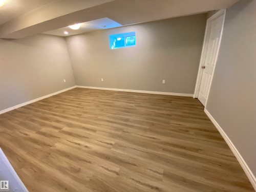 Spacious room featuring wood-finish flooring, light grey walls, white baseboards, and a white interior door - 12010 66 Street Nw, Edmonton, AB - Indoor Photo Showing Other Room