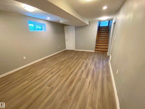 Spacious lower-level room featuring wood-finish flooring, recessed lighting, and a white interior door - 12010 66 Street Nw, Edmonton, AB - Indoor Photo Showing Basement