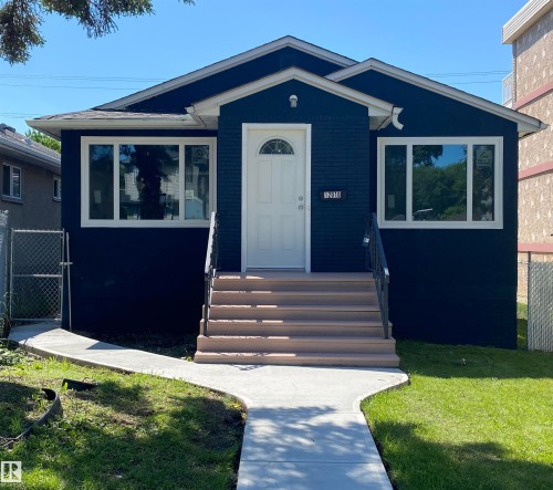 Front exterior showcasing a dark-hued facade with white trim, a white front door with an arched window, and a concrete walkway - 12010 66 Street Nw, Edmonton, AB - Outdoor