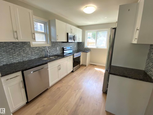 Contemporary kitchen featuring white cabinetry, dark granite-style countertops, and a subway tile backsplash - 12010 66 Street Nw, Edmonton, AB - Indoor Photo Showing Kitchen With Double Sink