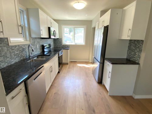 Kitchen featuring light wood-finish flooring, white cabinetry, dark granite-style countertops, mosaic tile backsplash, and stainless-steel appliances - 12010 66 Street Nw, Edmonton, AB - Indoor Photo Showing Kitchen With Double Sink With Upgraded Kitchen