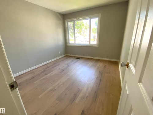 Bright room featuring wood-finish flooring, light gray wall paint, white baseboards, and a large window with white framing - 12010 66 Street Nw, Edmonton, AB - Indoor Photo Showing Other Room