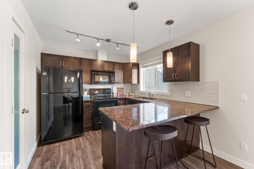 Kitchen featuring dark wood cabinetry, black appliances, a U-shaped countertop, and wood-finish flooring - #18 7289 South Terwillegar Dr Nw, Edmonton, AB - Indoor Photo Showing Kitchen