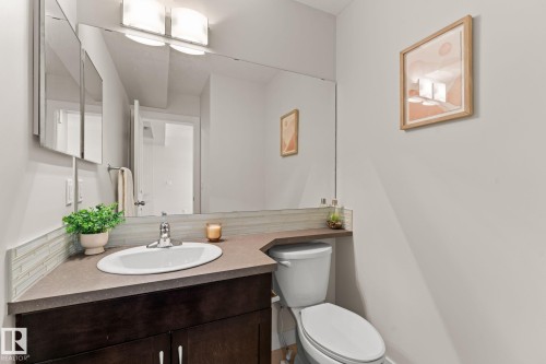 Bathroom featuring a dark wood-finish vanity, an integrated sink, a large wall mirror, and a white toilet - #18 7289 South Terwillegar Dr Nw, Edmonton, AB - Indoor Photo Showing Bathroom