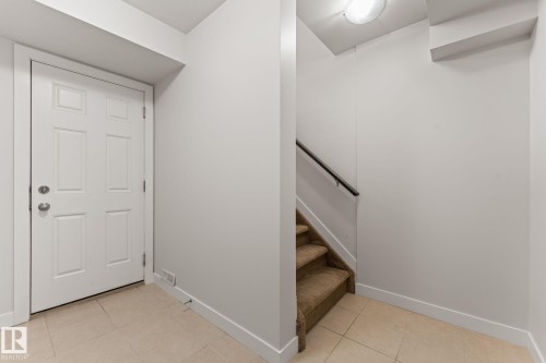 Tiled entry featuring a six-panel door with brushed nickel hardware, neutral wall tones, and a carpeted staircase with a dark handrail - #18 7289 South Terwillegar Dr Nw, Edmonton, AB - Indoor Photo Showing Other Room