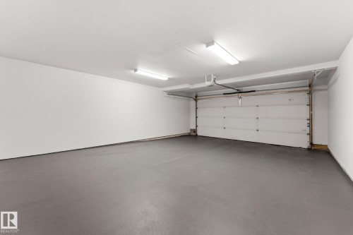 Spacious garage featuring a concrete floor, bright overhead lighting, and a roll-up garage door with an automatic opener - #18 7289 South Terwillegar Dr Nw, Edmonton, AB - Indoor Photo Showing Garage