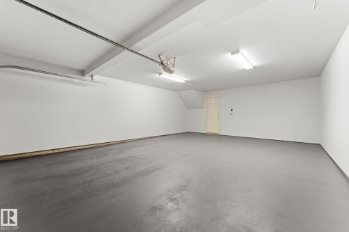 Spacious garage featuring a light gray concrete floor, white painted walls, and overhead fluorescent lighting - #18 7289 South Terwillegar Dr Nw, Edmonton, AB - Indoor Photo Showing Garage
