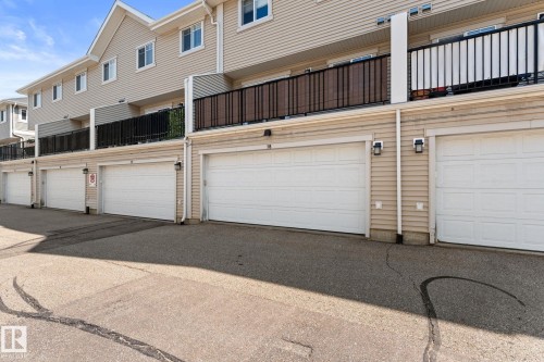 Townhome exterior featuring individual garages with white panel doors, beige siding, and black balcony railings - #18 7289 South Terwillegar Dr Nw, Edmonton, AB - Outdoor With Exterior