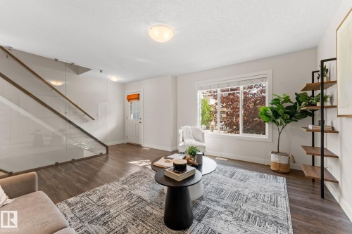 Living area featuring wood-finish flooring, a contemporary glass and wood staircase, bright white walls, a large window, and recessed lighting - #18 7289 South Terwillegar Dr Nw, Edmonton, AB - Indoor Photo Showing Living Room