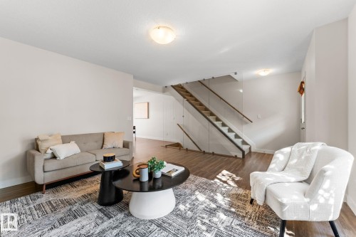 Living area with wood-finish flooring, light-toned walls, and a contemporary glass and wood staircase - #18 7289 South Terwillegar Dr Nw, Edmonton, AB - Indoor Photo Showing Living Room