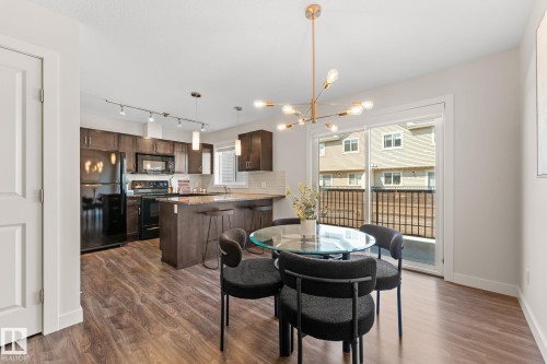 Open-concept living space featuring wood-finish flooring, a contemporary kitchen with dark cabinetry, black appliances, and a breakfast bar - #18 7289 South Terwillegar Dr Nw, Edmonton, AB - Indoor Photo Showing Other Room