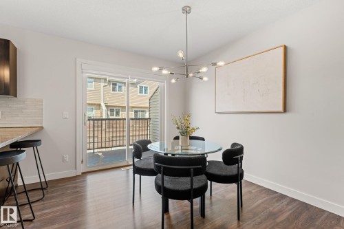 Open-concept dining area featuring wood-finish flooring, a contemporary ceiling light fixture, a sliding glass door providing access to an exterior balcony, and a breakfast bar with a light-toned countertop and tile backsplash - #18 7289 South Terwillegar Dr Nw, Edmonton, AB - Indoor Photo Showing Dining Room