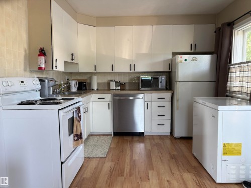 Kitchen featuring white cabinetry with black hardware, wood-finish flooring, a stainless steel dishwasher, a white electric range, and a white refrigerator - 4901 53 Avenue, Elk Point, AB - Indoor Photo Showing Kitchen