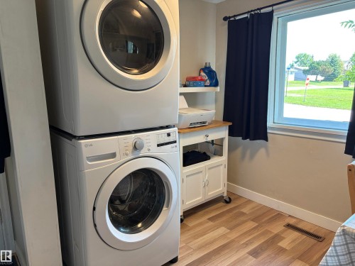 Laundry area featuring a stacked washer and dryer, wood-finish flooring, and a window with natural light - 4901 53 Avenue, Elk Point, AB - Indoor Photo Showing Laundry Room