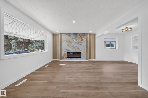 Spacious living area featuring wide plank wood-finish flooring and a modern electric fireplace with a decorative surround - 5204 97A Avenue Nw, Edmonton, AB - Indoor With Fireplace
