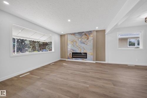 Spacious living area featuring an electric fireplace with a decorative stone-look surround and vertical wood panel accents - 5204 97A Avenue Nw, Edmonton, AB - Indoor With Fireplace