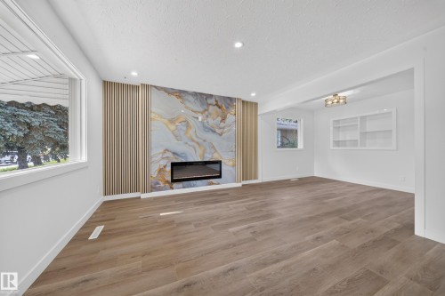 Spacious room featuring wood-finish flooring, a contemporary fireplace with a decorative stone-look surround, slatted wood paneling, recessed lighting, and built-in shelving - 5204 97A Avenue Nw, Edmonton, AB - Indoor With Fireplace