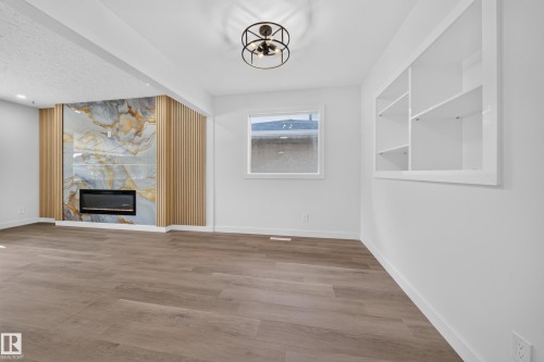 Contemporary room featuring a decorative fireplace with a large-format veined panel and vertical wood slat accents - 5204 97A Avenue Nw, Edmonton, AB - Indoor With Fireplace