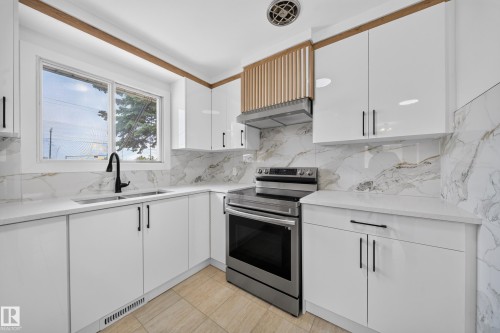 Modern kitchen featuring white cabinetry with matte black hardware, stone-finish countertops, and a coordinating full-height backsplash - 5204 97A Avenue Nw, Edmonton, AB - Indoor Photo Showing Kitchen