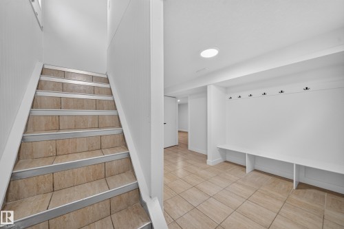 Staircase with tile treads and metal nosing, complemented by a built-in bench seating area with storage cubbies and wall-mounted coat hooks - 5204 97A Avenue Nw, Edmonton, AB - Indoor Photo Showing Other Room