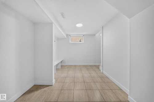 Finished lower-level space featuring light-toned tile flooring, painted white walls, and a built-in bench - 5204 97A Avenue Nw, Edmonton, AB - Indoor Photo Showing Other Room
