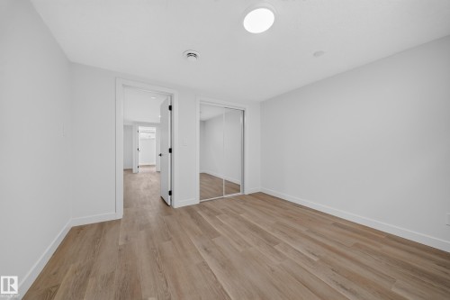 Spacious room featuring wood-finish flooring, white walls, and a full-height mirrored closet - 5204 97A Avenue Nw, Edmonton, AB - Indoor Photo Showing Other Room