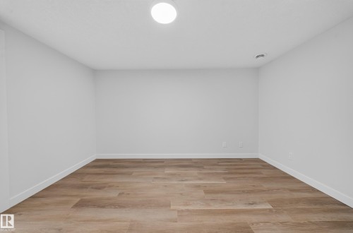 Spacious room featuring wood-finish flooring, white walls, and a ceiling-mounted light fixture - 5204 97A Avenue Nw, Edmonton, AB - Indoor Photo Showing Other Room