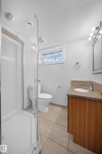 Bathroom featuring a stand-up shower, single vanity with a stone countertop, and tile flooring - 5204 97A Avenue Nw, Edmonton, AB - Indoor Photo Showing Bathroom