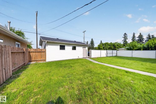 Spacious backyard featuring a detached garage with white siding, a concrete pathway, a wood privacy fence, and a white vinyl fence - 5204 97A Avenue Nw, Edmonton, AB - Outdoor