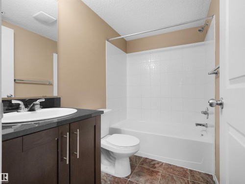 Full bathroom featuring a dark wood-finish vanity with a white oval sink and chrome faucet, a white toilet, and a white tub with white subway tile surround - #109 3207 James Mowatt Tr Sw, Edmonton, AB - Indoor Photo Showing Bathroom