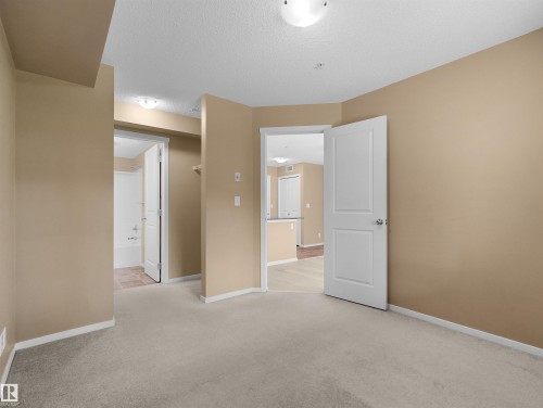 Carpeted room featuring neutral wall tones, white trim, a flush-mount ceiling light, and access to a bathroom with a white tub and a separate area with wood-finish flooring - #109 3207 James Mowatt Tr Sw, Edmonton, AB - Indoor Photo Showing Other Room