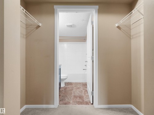 Carpeted entryway featuring two wire shelving units - #109 3207 James Mowatt Tr Sw, Edmonton, AB - Indoor