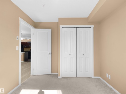 Neutral-toned room featuring light-colored carpeting, a white bi-fold closet door, and a white interior door - #109 3207 James Mowatt Tr Sw, Edmonton, AB - Indoor