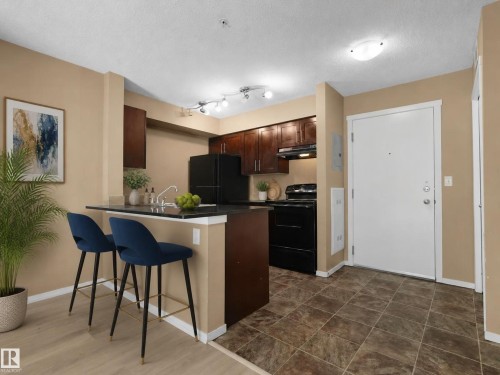 Kitchen featuring dark wood cabinetry, black appliances, and a breakfast bar with a contrasting countertop - #109 3207 James Mowatt Tr Sw, Edmonton, AB - Indoor Photo Showing Kitchen