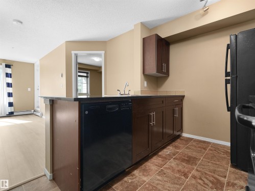 Kitchen featuring dark wood-finish cabinetry, black appliances, and a built-in dishwasher - #109 3207 James Mowatt Tr Sw, Edmonton, AB - Indoor Photo Showing Kitchen