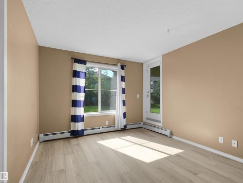 Light wood-finish flooring complements neutral wall tones in this living space - #109 3207 James Mowatt Tr Sw, Edmonton, AB - Indoor Photo Showing Other Room