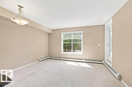 Expansive interior space featuring light-colored carpeting, a large window with blinds, and a glass-paneled door - #119 111 Watt Cm Sw, Edmonton, AB - Indoor Photo Showing Other Room