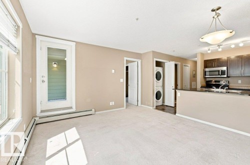 Open-concept living area with light-colored carpeting, a full-light glass door leading to an outdoor space, and a functional kitchen - #119 111 Watt Cm Sw, Edmonton, AB - Indoor Photo Showing Kitchen