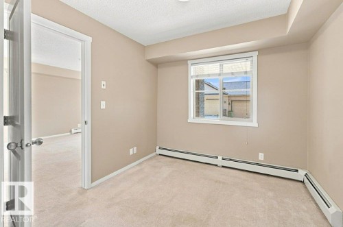 Carpeted room featuring a single window with horizontal blinds, neutral wall paint, white trim, and baseboard heating - #119 111 Watt Cm Sw, Edmonton, AB - Indoor Photo Showing Other Room