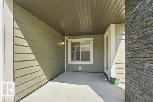 Covered patio featuring a concrete slab, sage green siding, and a stacked stone column - #119 111 Watt Cm Sw, Edmonton, AB - Outdoor With Exterior